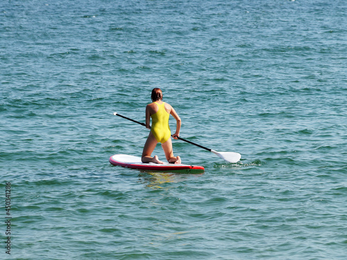 teenage girl riding a sup-board in the sea on her knees