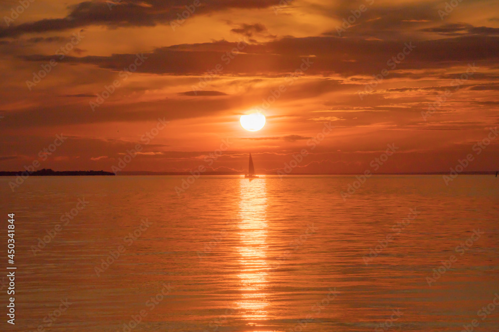 A small sailing yacht crosses a strip of light on the surface of the water.