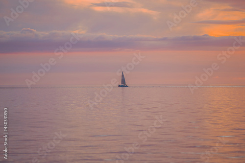 A small sailing yacht is drifting off the coast in the soft illumination of the sun that has already set.