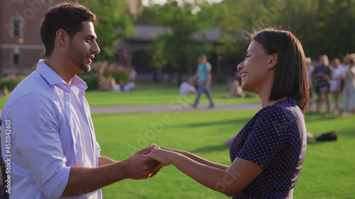 Side view of smiling young multiethnic couple holding hands in summer park