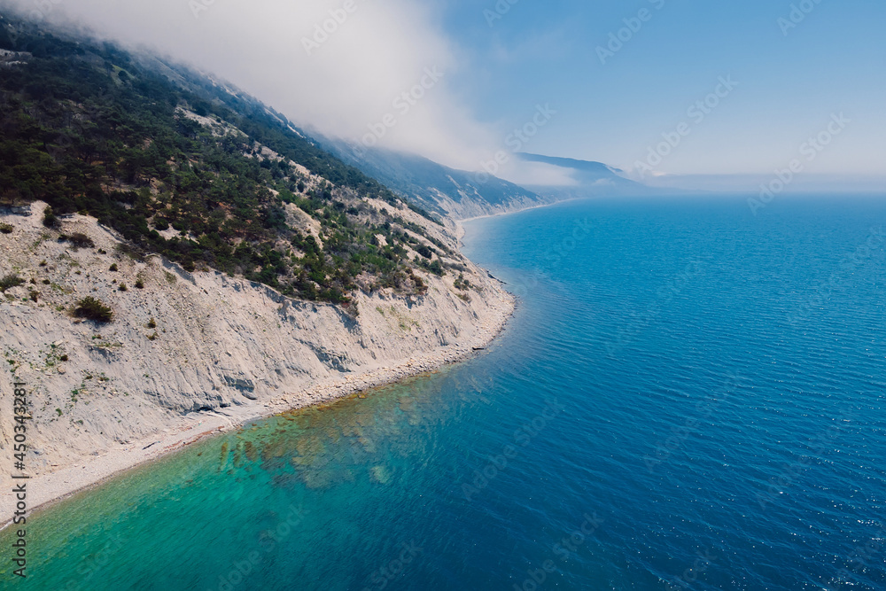 Aerial view of rocky coastline with clouds and blue sea.