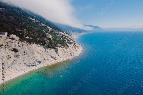 Aerial view of rocky coastline with clouds and blue sea.
