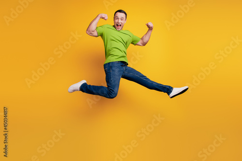 Portrait of funky winner guy jump show biceps muscle on yellow wall