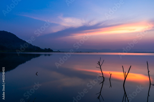 Twilight sun shines upon the clouds as a reflection of the water surface, with branches in the background, with mountains and the night sky in the background.
