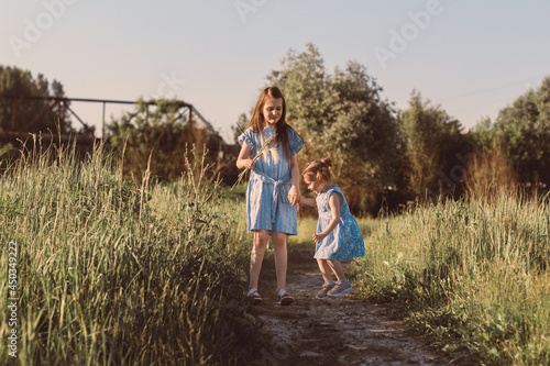 Little girl jumping in summer grass field with scenic path. Two sisters walking together and enjoy calm sunny day.