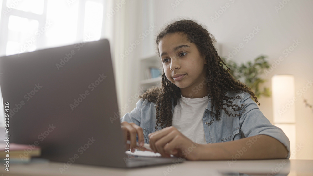Afro-american teen girl doing homework online, looking at screen skeptically Afro-american teen girl doing homework online, looking at screen skeptically