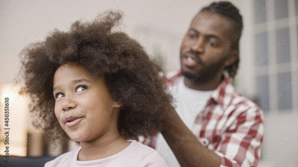 Naklejka premium Happy father combing afro hair of little daughter, morning routine, family