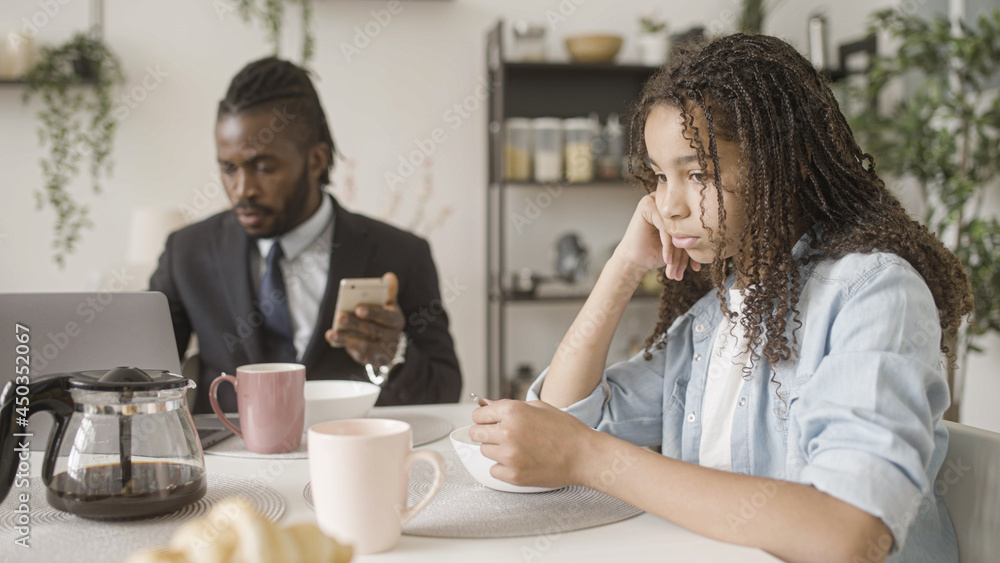 Sad black teenage girl sitting next to busy father working in the morning, loneliness Sad black teenage girl sitting next to busy father working in the morning, loneliness