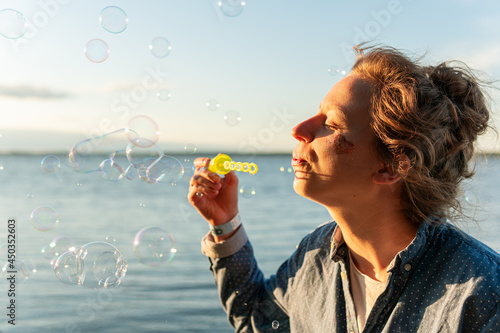 Happy woman is blowing bubbles in front of sea on a warm sunny summer day