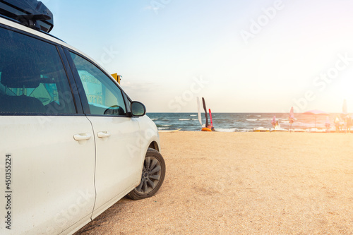 Side view of big family white suv van car with big rooftop cargo rack box at scenic sand seaside campsite camp coast of sea or ocean sky on background. Accessory rental travel trip vacation concept