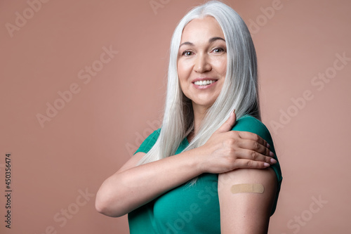 Bild auf Leinwand Happy vaccinated mature female showing shoulder with adhesive plaster after immunization vaccine