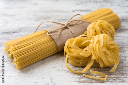 Uncooked spaggetti wrapped in brown paper and tied with twine, fettuccini on a light rustic background photo