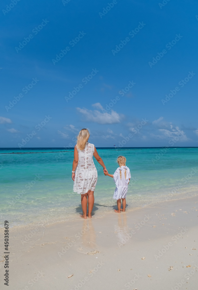 Beautiful mother and little daughter watching on the ocean from the tropical Maldivian beach. Crossroads Maldives, july 2021