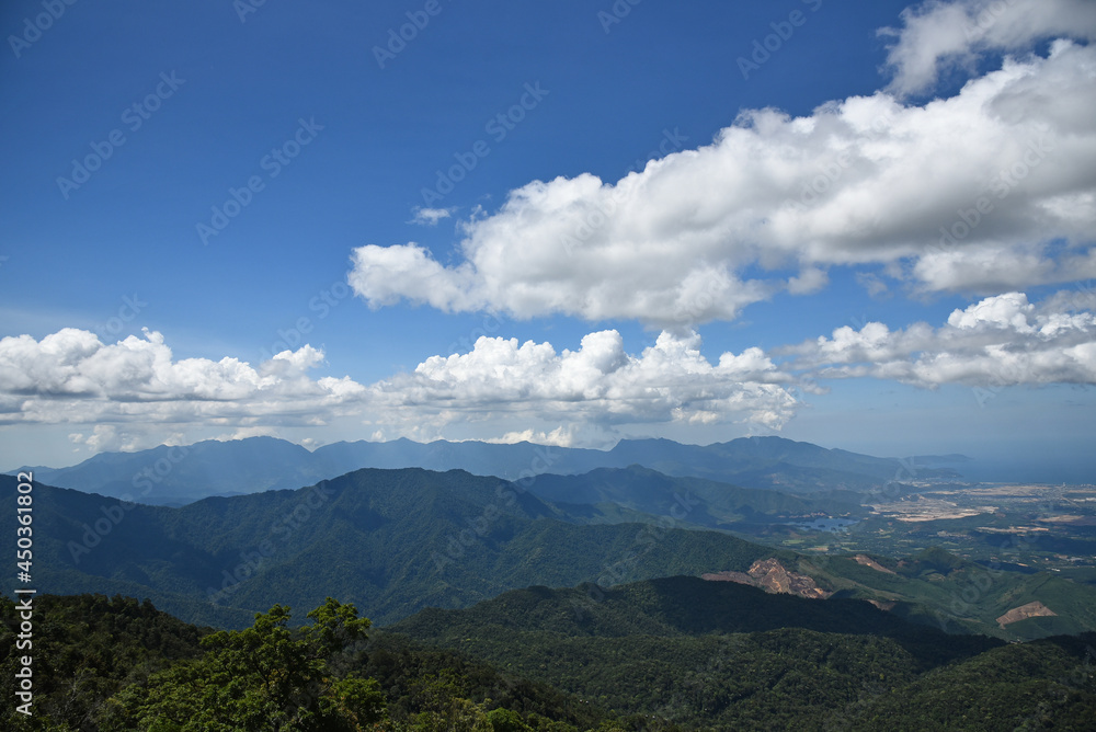 view from a mountain to a valley with a city illuminated by the sun, under clouds, many trees and greenery