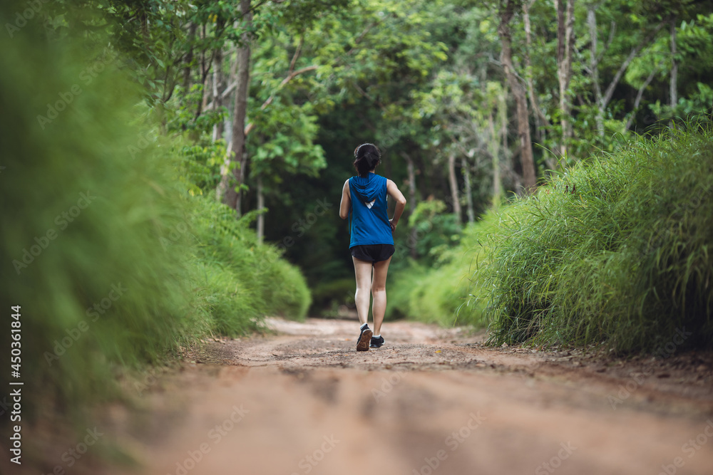 Behind active woman trail runner running in park outdoor. Trail running athlete through the in the rural road and tropical. Woman running in the park. Behind active woman trail runner running in park outdoor. Trail running athlete through the in the rural road and tropical. Woman running in the park.