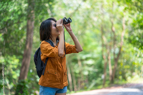 Young asian woman backpacker with binoculars telescope looking birds in forest on holidays vacation in summer,Adventure travel concept