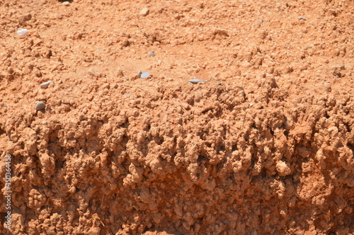 Red and brown sand, dirt and stones texture of a eroded desert beach, with hard sun light