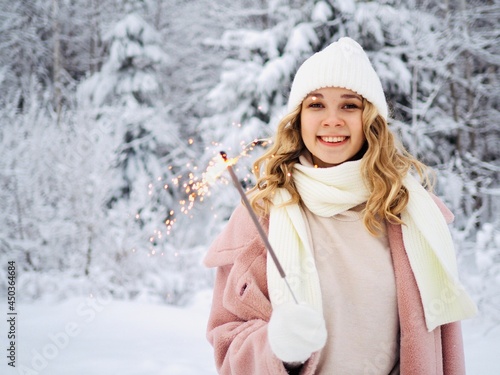 Portrait of smiling girl wearing white knitted hat, scarf, mittens and sweater with sparkler in winter time outdoors. Christmas holidays © Alyona Shu
