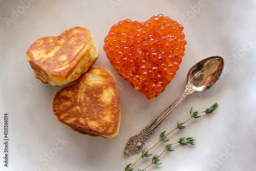 Heart shaped red caviar and pancreas, spoon and thyme sprigs over green plate.