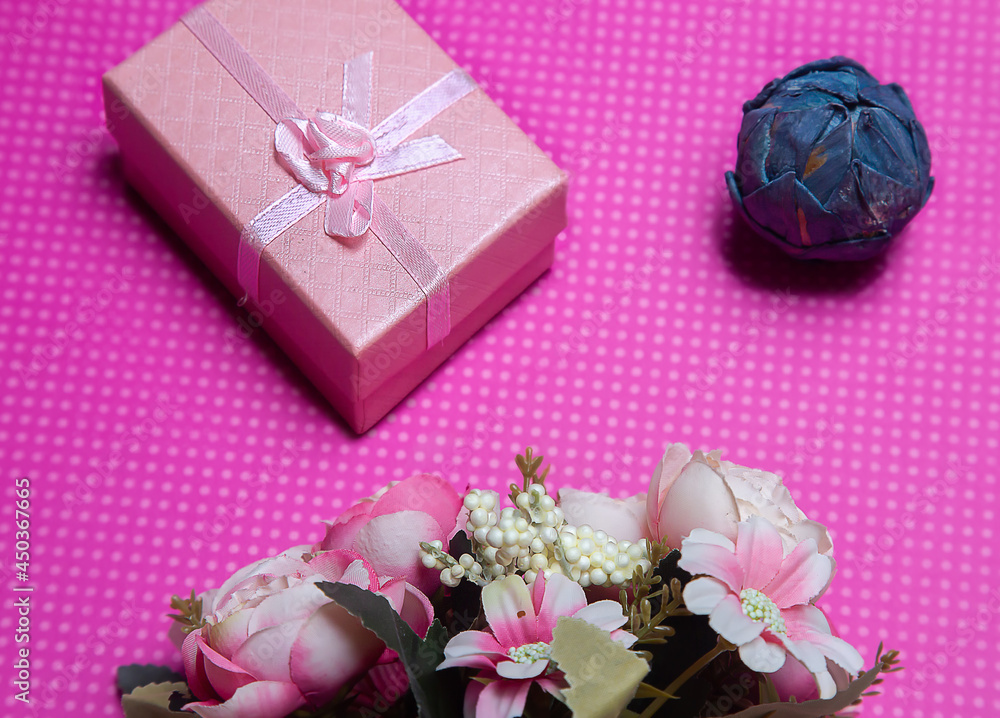 A flat lay photo of a bouquet of flowers, a gift in the form of a box and accessories on a pink background top view. High quality photo