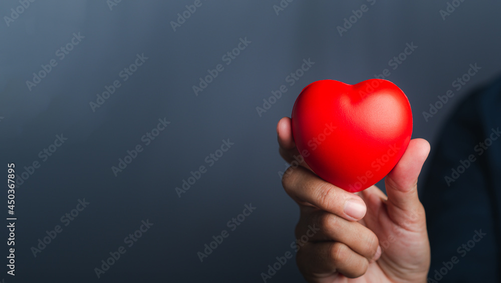 Hand of holding red heart shape against a gray background. Close-up photo. Sign of love, healthcare, valentine's day, world heart day concept Hand of holding red heart shape against a gray background. Close-up photo. Sign of love, healthcare, valentine's day, world heart day concept