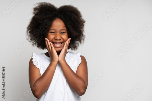 Happy surprised child emotions. Portrait of adorable little girl holding hands on face and smiling in amazement, keeping mouth wide open, shocked expression. Studio shot isolated on white background