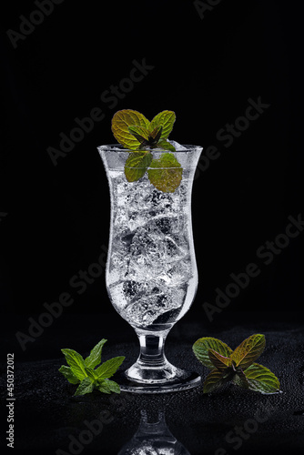Cocktail with mint in a cocktail glass with ice on a misted surface and a black background. Refreshing drink with ice and mint. In a low key. Free space on top.