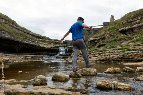 man walking on stones of river balancing