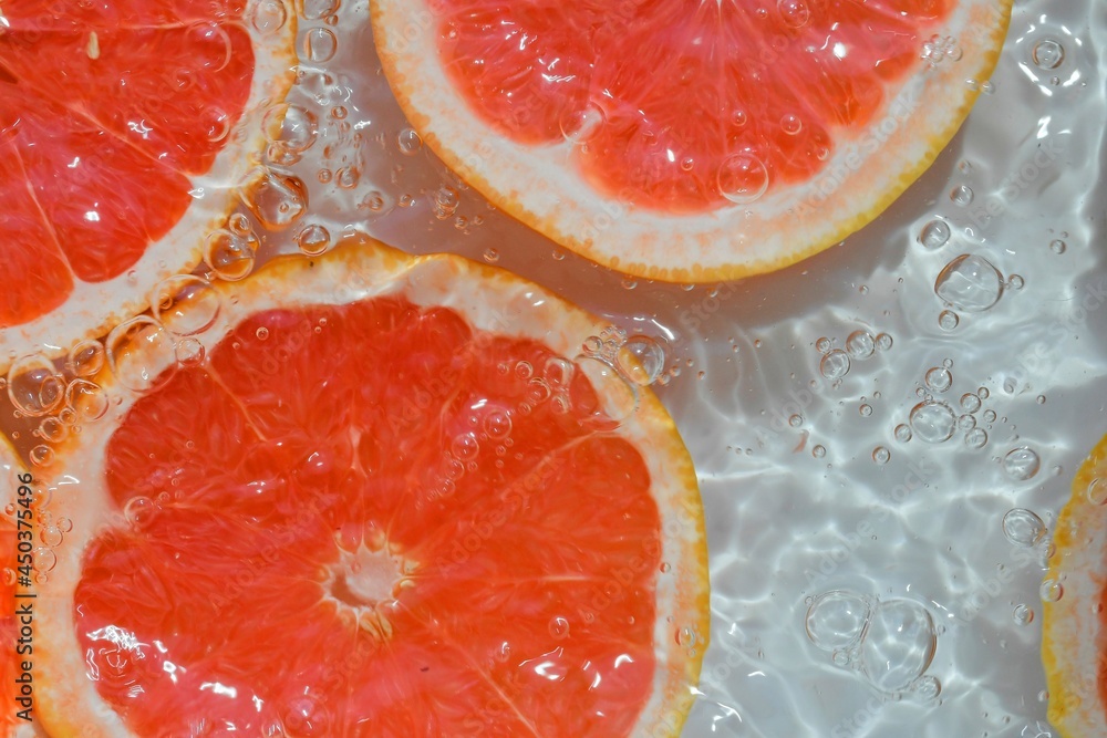 Slices of grapefruit in water on white background. Grapefruit close-up in liquid with bubbles. Slices of blood red ripe grapefruit in water. Macro image of fruits in water Slices of grapefruit in water on white background. Grapefruit close-up in liquid with bubbles. Slices of blood red ripe grapefruit in water. Macro image of fruits in water