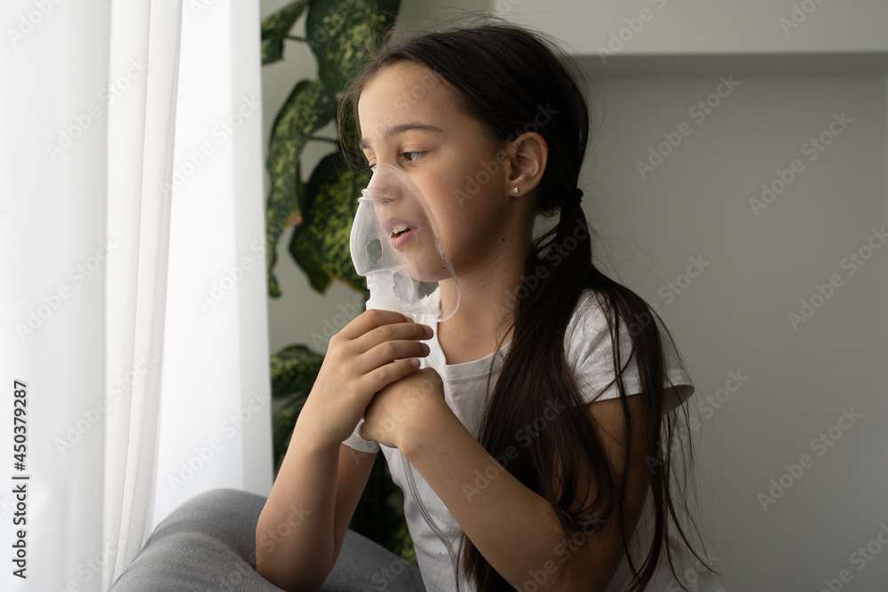 Kid girl makes inhalation with a nebulizer. sick child holding inhalator in hand and breathes through an inhaler at home Kid girl makes inhalation with a nebulizer. sick child holding inhalator in hand and breathes through an inhaler at home