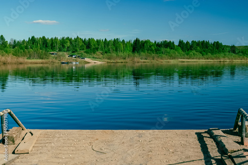 The back of the ferry with a view of a summer landscape with a river, a blue sky with clouds, and the shore
