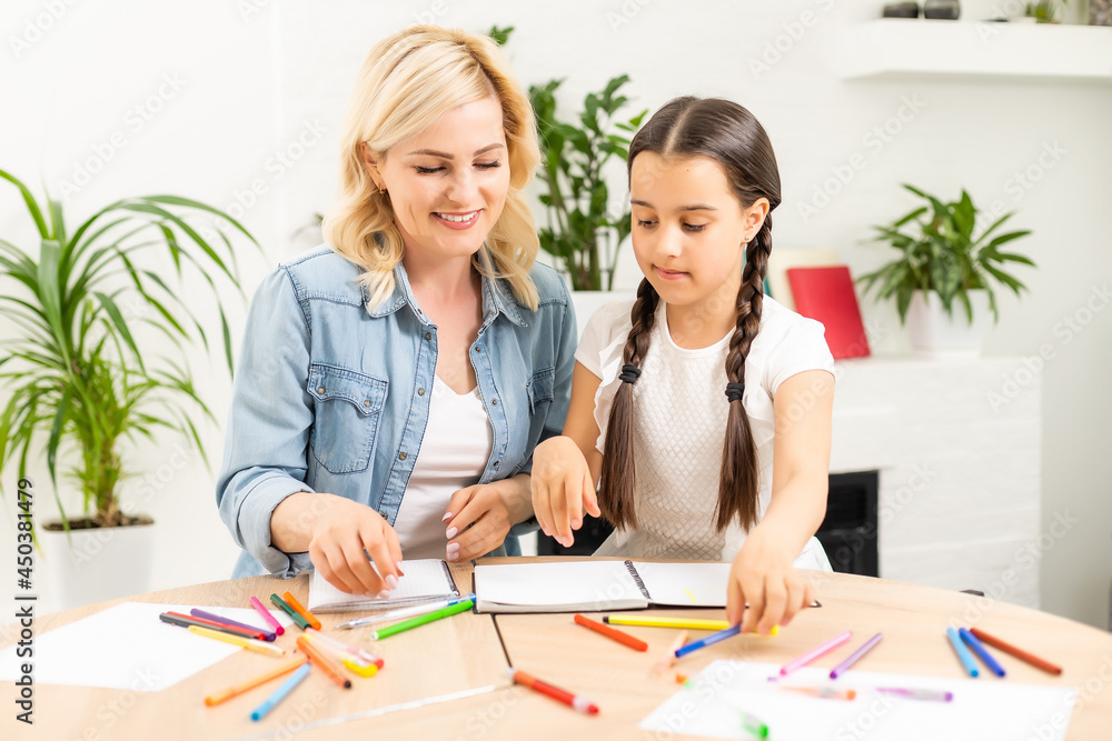 Mother and daughter beautiful and happy make a card for mother's day sitting together at the table with paper and pencils Mother and daughter beautiful and happy make a card for mother's day sitting together at the table with paper and pencils