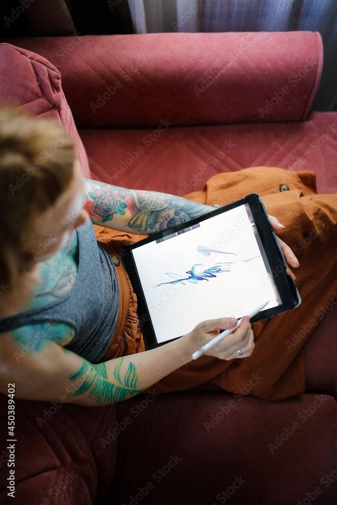 Cute red-haired girl artist draws on a tablet in a cozy living room in a real interior, top view of the tablet screen close-up,