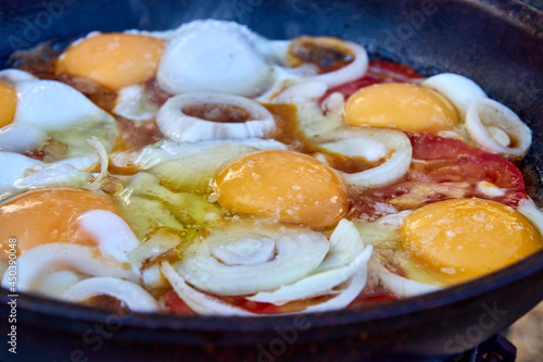 close-up of frying eggs with onions and tomatoes in a frying pan. picnic in nature