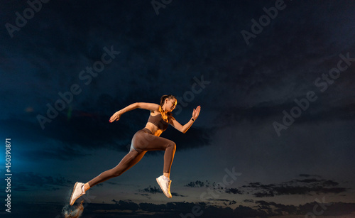 Sprinter run. Strong athletic woman running on black background wearing in the sportswear. Fitness and sport motivation. Runner concept. © Mike Orlov