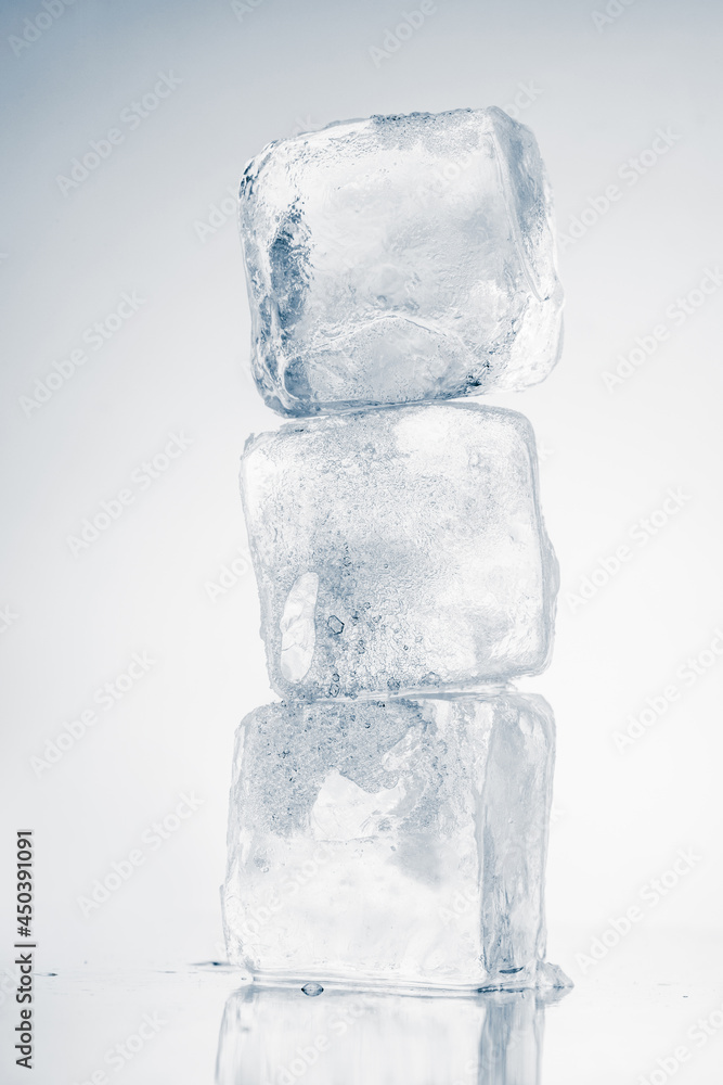 The vertical stack of three ice cubes on white background with reflection. The vertical stack of three ice cubes on white background with reflection.
