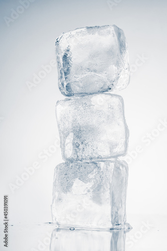 The vertical stack of three ice cubes on white background with reflection.