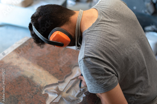 Fototapet Caucasian man sculptor, bush hammering a granite headstone in a workshop, work c