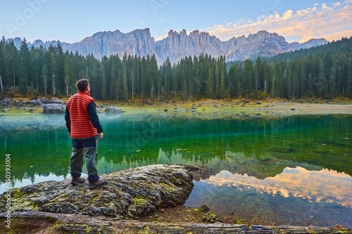 man stands on a stone by the lake, watching the sunrise over the mountains
