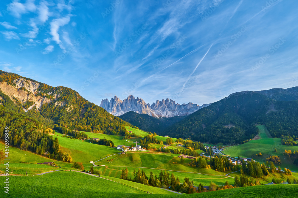 Amazing autumn scenery in Santa Maddalena village with church, colorful trees and meadows under rising sun rays. Dolomite Alps, Italy.