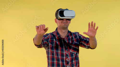 Cheerful young man are amazed with using VR goggles. There is yellow background.