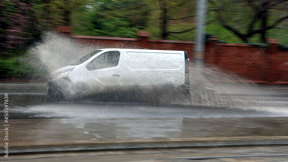 Samochód w czasie ulewy wpada w kałużę wody na jezdni powodując rozbryzg. - obrazy, fototapety, plakaty 