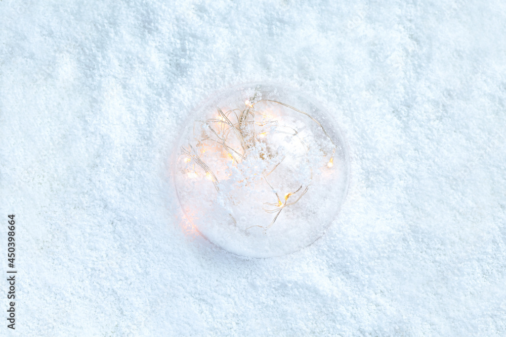 A transparent ball with a garland glows with a yellow light and lies on the snow A transparent ball with a garland glows with a yellow light and lies on the snow