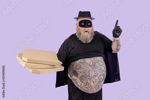 Bellicose fat man in Zorro costume with boxes of pizza stands on