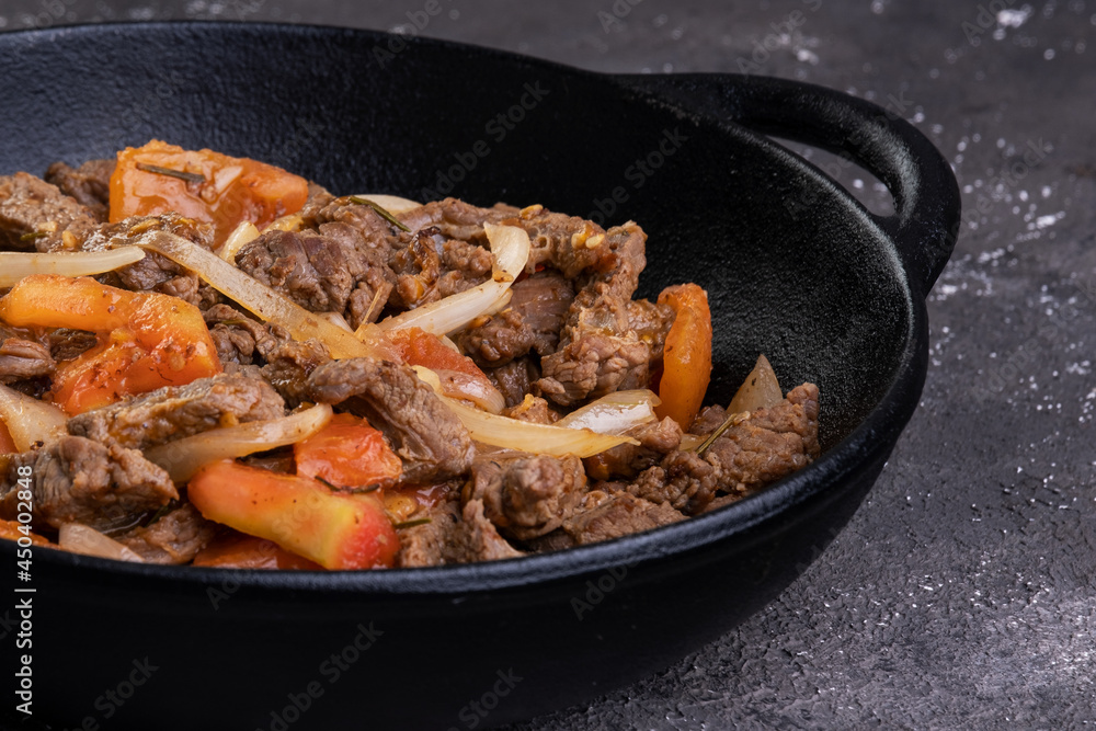 Sliced and fried filet mignon with tomato and onion in an iron skillet Sliced and fried filet mignon with tomato and onion in an iron skillet