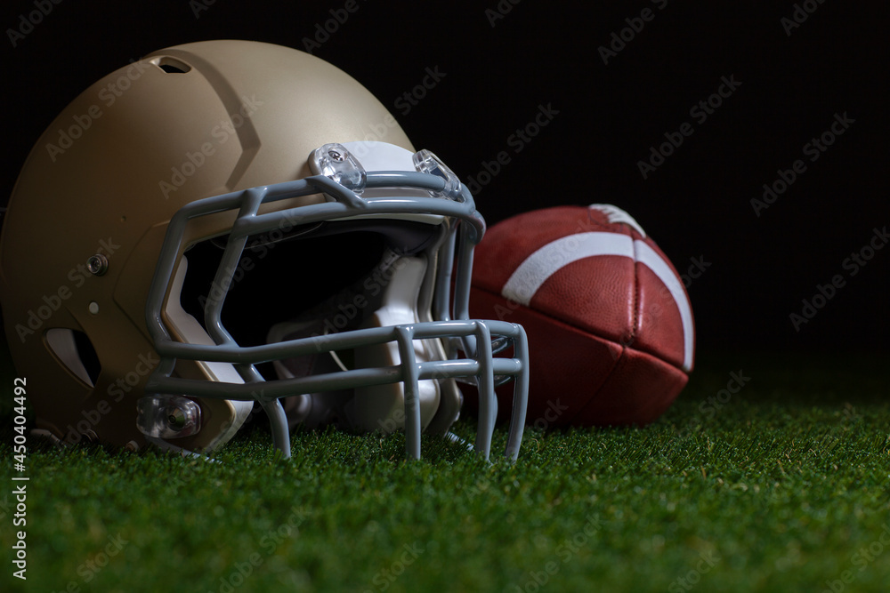 Naklejka Low angle selective focus of football and gold helmet on grass with dark background