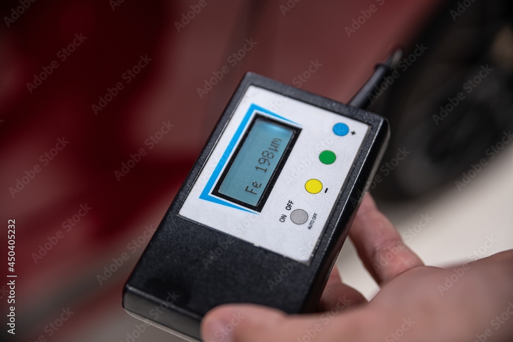 Man checking car paint thickness with electronic meter