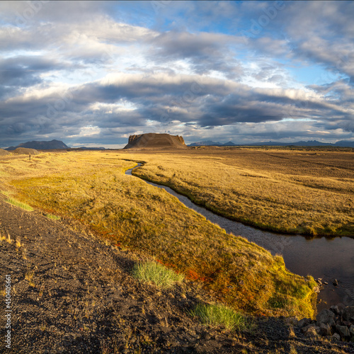 River flows among orange dry grass field to mountain in Iceland under blue sky
