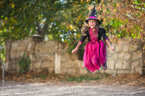 A little girl in a witch costume is jumping on the street. Halloween holiday. Copy space