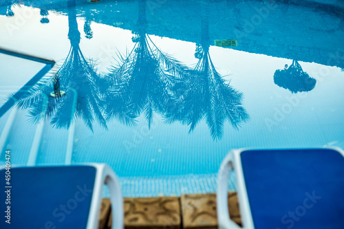 Fototapeta Naklejka Na Ścianę i Meble -  Closeup sunloungers and swimming pool with reflected palms in water
